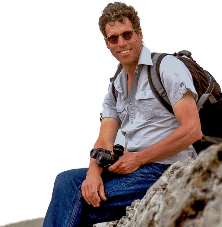 David P. Mindell sitting on a rock with binoculars